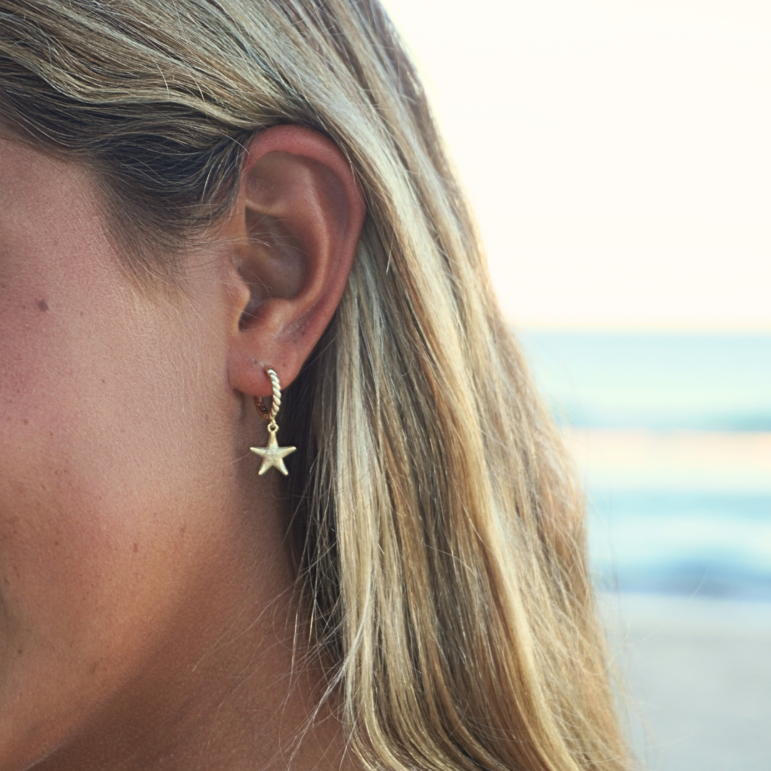 Close up of ear with surf girl wearing Seastar starfish Gold Pendant Earrings at beach. Waterproof Kailumea