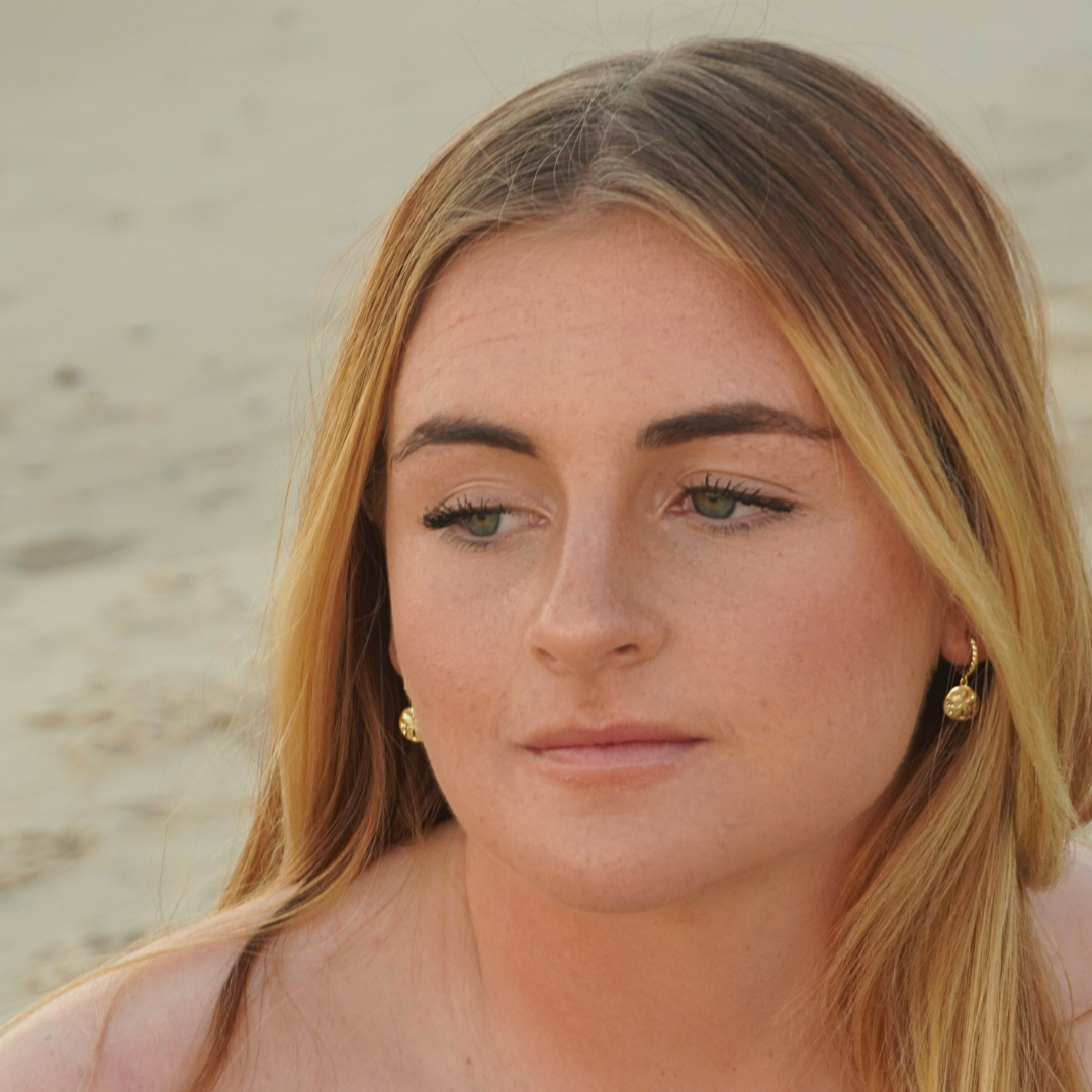 Woman wearing Isla Gold Sand Dollar Hoop earrings on the beach. Waterproof Kailumea