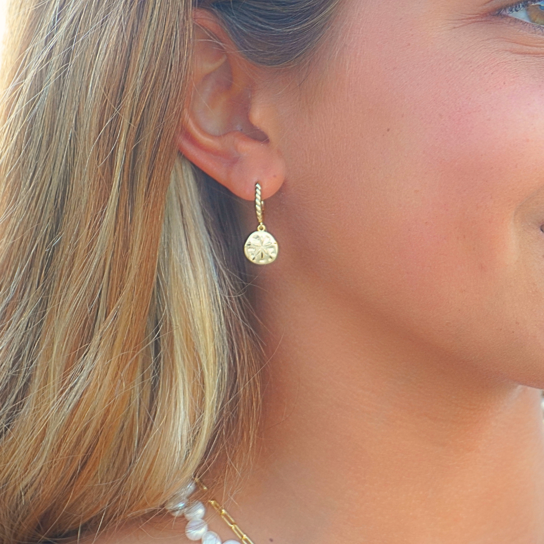Close up on ear, surf girl wearing Isla Gold sand dollar hoop earrings on beach. waterproof Kailumea