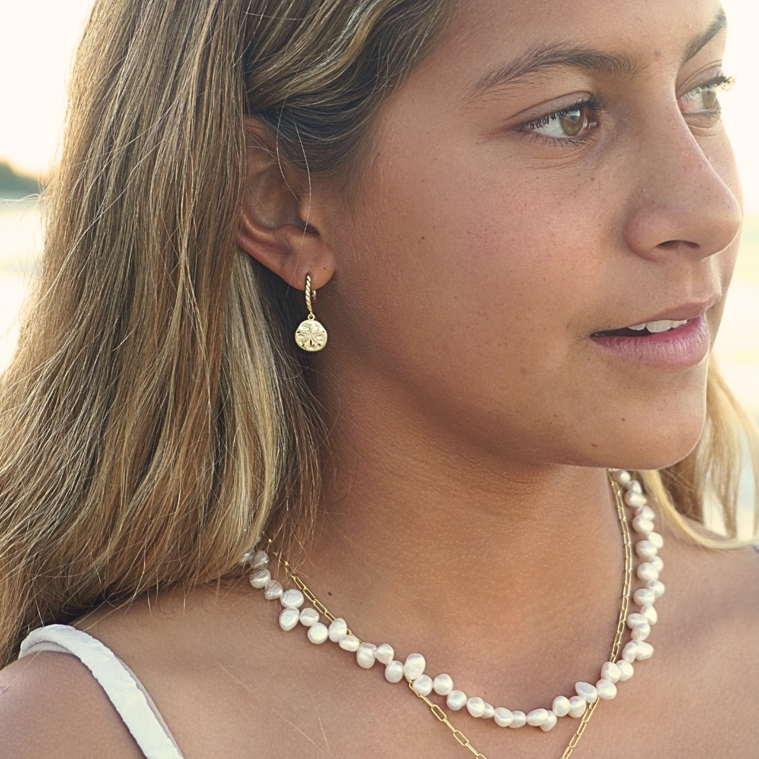 Woman wearing Isla Gold Sand Dollar Hoop earrings and Luna Tide necklace on the beach. Waterproof Kailumea
