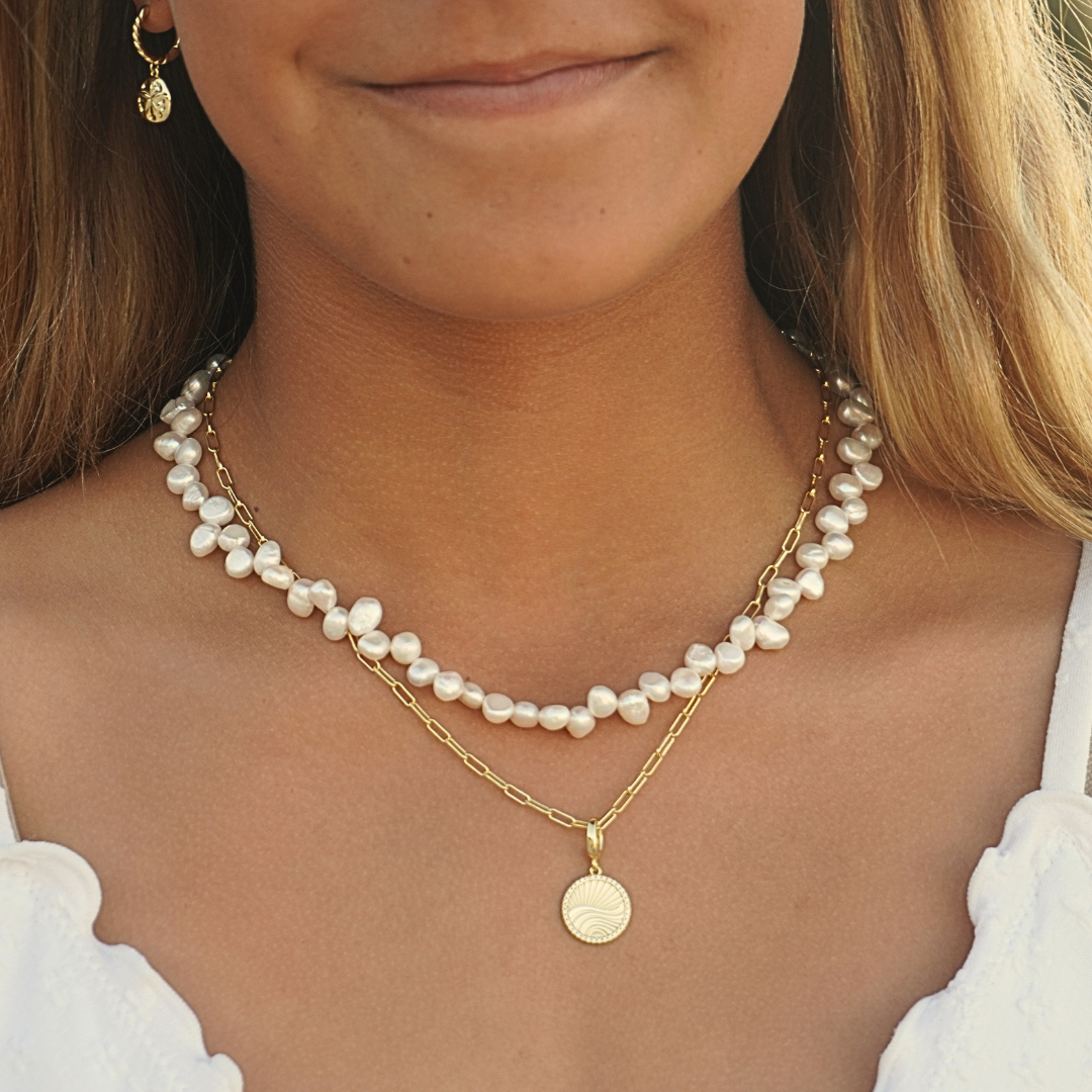 Woman wearing Isla Gold Sand Dollar Hoop earrings , Luna tide necklace and Aurora necklace stacked on the beach. Waterproof Kailumea