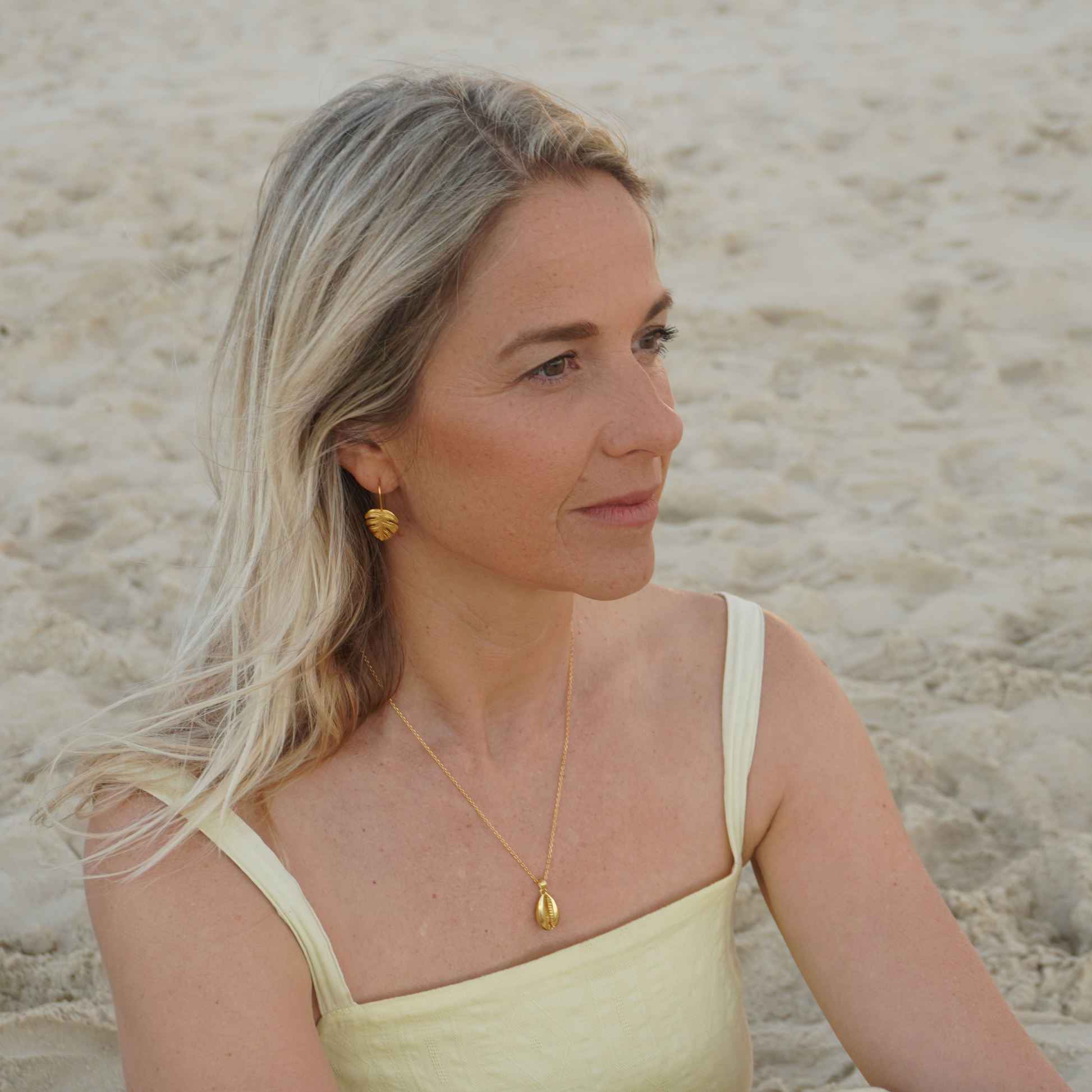 Woman wearing Gold Waterproof La Isla Threads Monstera Leaf Thread Earrings on the beach Kailumea