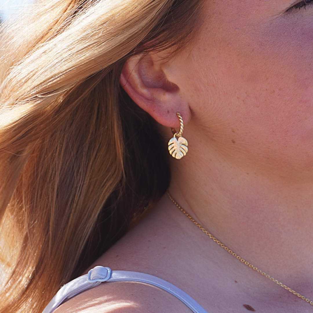 Close up in ear Woman wearing the Mahina Gold Monstera leaf pendant hoop earring at beach waterproof Kailumea