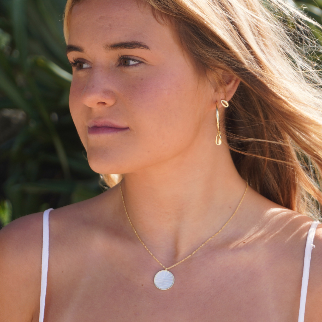 Woman wearing Large Gold Cali Hoops with cowrie pendant , gold cowrie stud earrings and Solaya necklace at the beach waterproof Kailumea