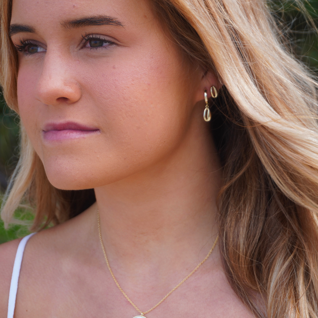 Woman wearing Gold Cowrie Pendant Hoop Earrings and Santorini Starfish necklace and gold cowrie stud earrings at the beach waterproof Kailumea