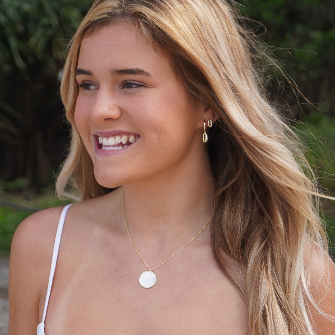 Woman wearing Gold Cowrie Pendant Hoop Earrings, cowrie gold stud earrings and Solaya necklace at the beach waterproof Kailumea