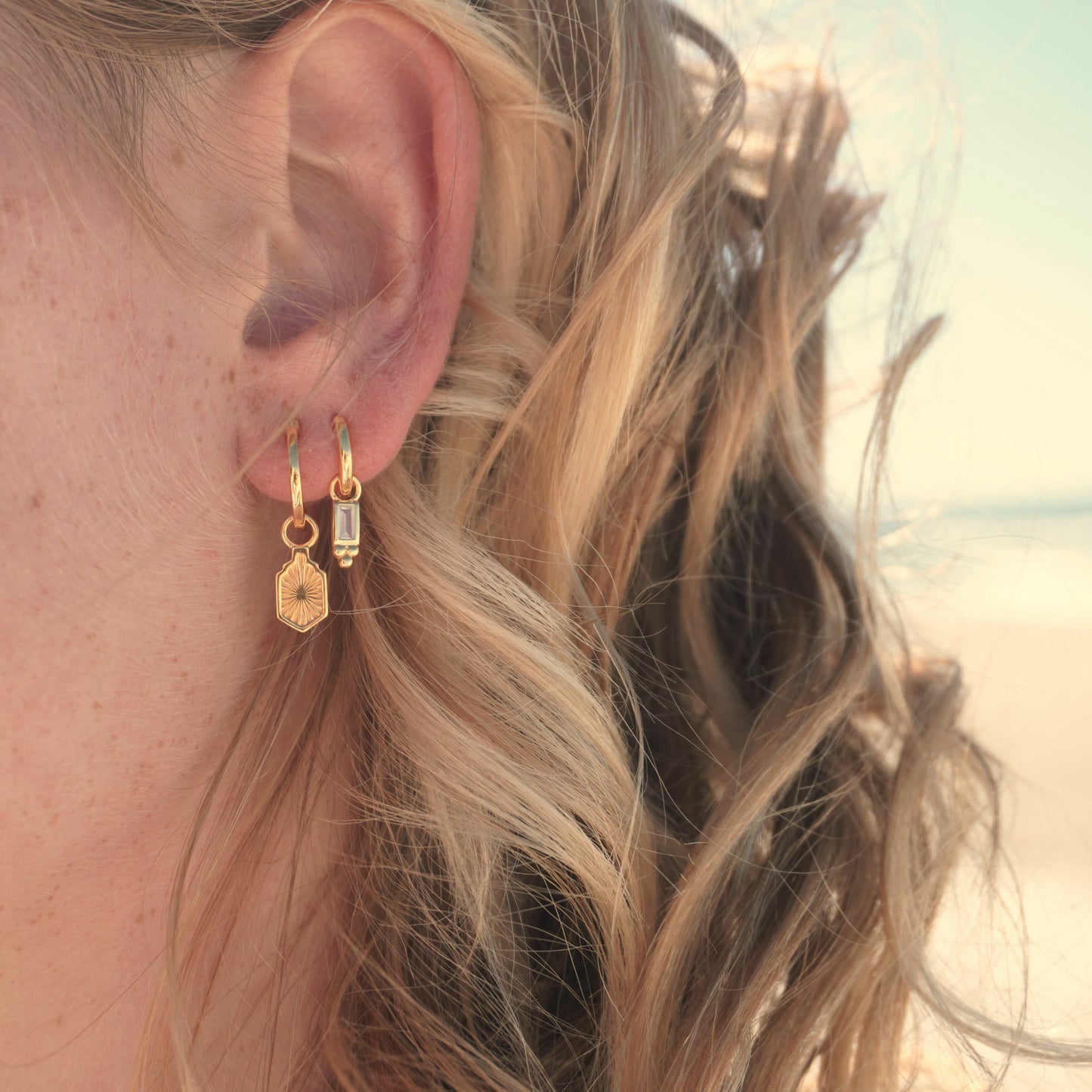 Close up in ear woman wearing Waterproof Manea Gold Boho Pendant Hoop Earrings and Pavana Huggie hoop earrings at beach Kailumea