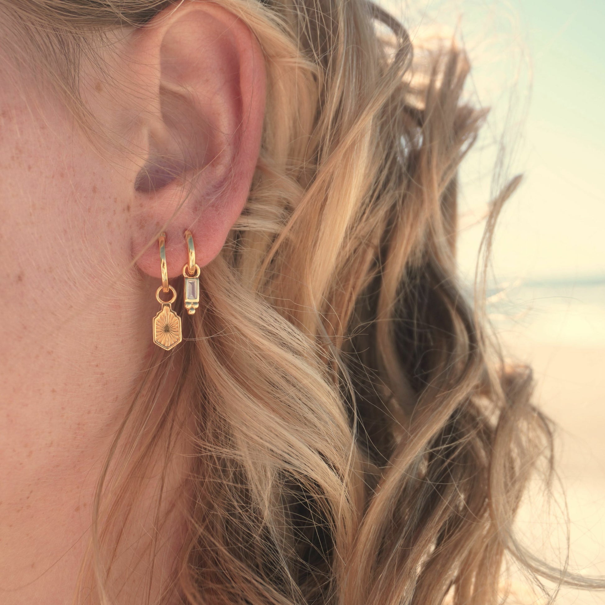 Close up in ear woman wearing Waterproof Manea Gold Boho Pendant Hoop Earrings and Pavana Huggie hoop earrings at beach Kailumea