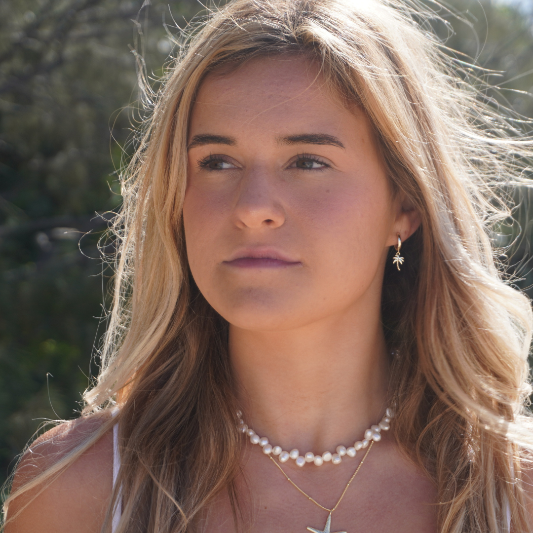 woman surf girl wearing palm tree earrings, Luna tide necklace and Santorini Necklace stacked at beach gold waterproof kailumea