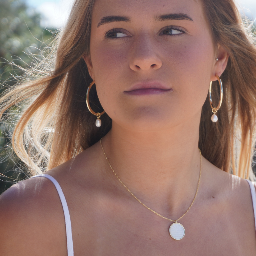 Woman wearing Waikiki Large Gold hoops with pearl charm pendant and Solaya Necklace at the beach. waterproof Kailumea